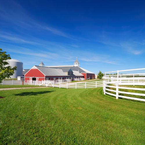 A farm surrounded by a white fence on a clear day.